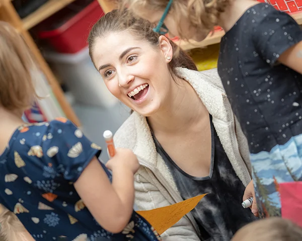 Student teacher sitting on floor smiling at two young children